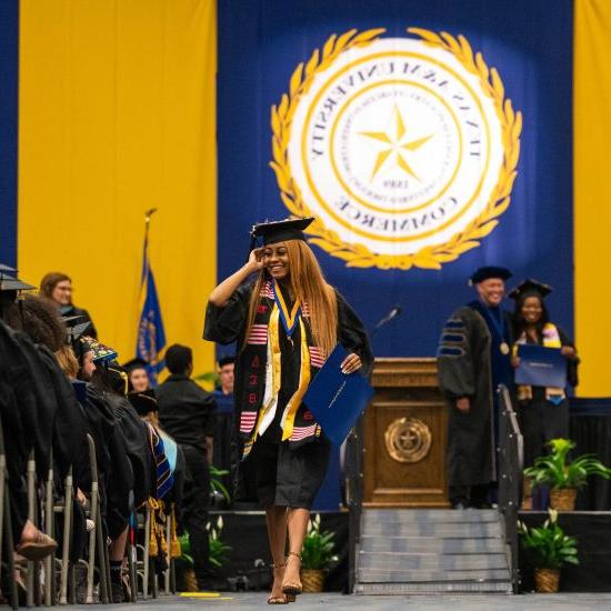 A female student walking down the graduation ceremony smiling.