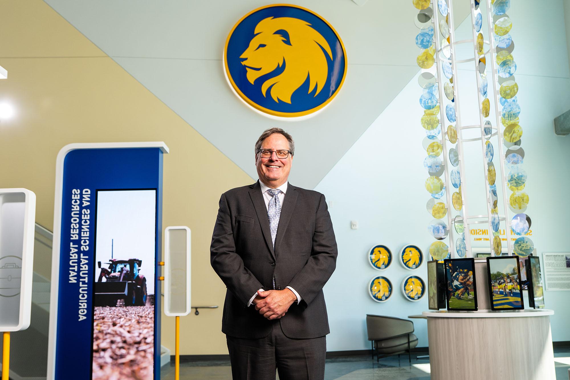 Dr. Mark Rudin, President of East Texas A&M University, standing in the Agricultural Sciences and Natural Resources building with the university logo in the background.